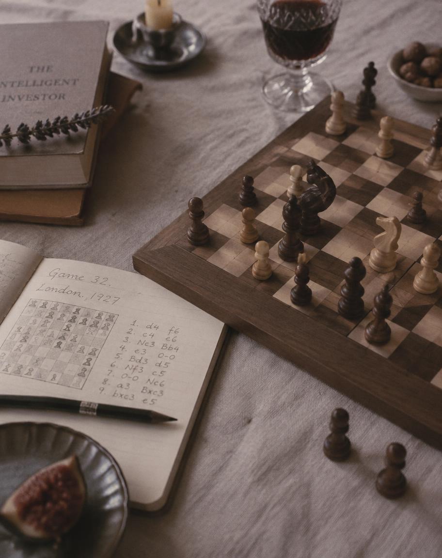 A wooden chess set mid game beside a notation notebook